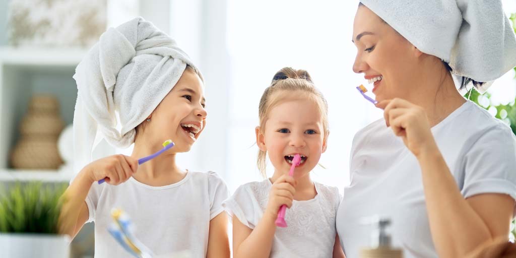 girls brushing teeth with mom